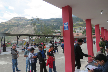 Alausí. Varias personas hacen fila en un recinto electoral. Al fondo, se observa la zona cero del derrumbe.
