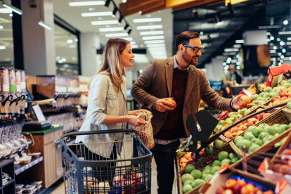 Young adult couple choosing some fresh fruits in grocery store, with shopping trolley beside them