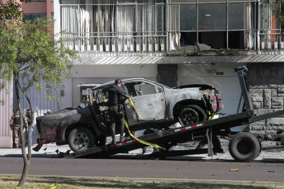 Un policía carga en una grúa los restos de un carro bomba que explotó en los exteriores del edificio del Servicio Nacional de Atención Integral a Personas Privadas de Libertad (SNAI), en Quito (Ecuador).