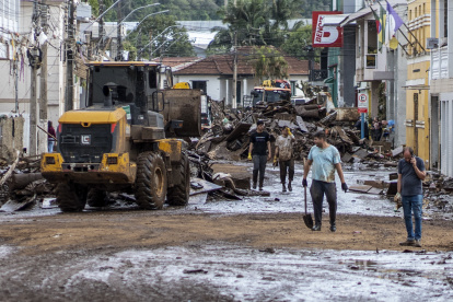Personas junto a un vehículo de maquinaria pesada mientras despejan una calle inundada por las torrenciales lluvias, en Muçum, estado de Rio Grande do Sul (Brasil).