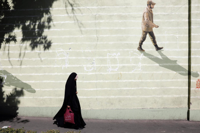 Imagen de archivo de una mujer con velo que pasa junto a una pared con un soldado iraní pintado en ella en una calle de Teherán.