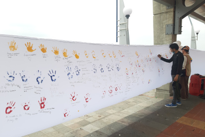 Personas acuden para dejar su huella de la mano en colores de la bandera sobre la lona y escribir un mensaje de paz