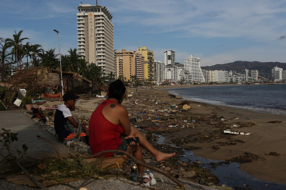 Personas permanecen sentadas junto a los escombros causados por el huracán Otis hoy, en el balneario de Acapulco, en el estado de Guerrero (México)