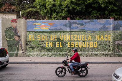 Un hombre conduce una moto frente a un mural que dice "El sol de Venezuela nace por el esequibo", el 2 de noviembre de 2023, en Caracas (Venezuela).
