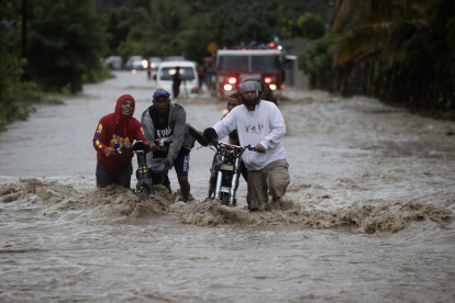 SAN JOSÉ DE OCOA (REPÚBLICA DOMINICANA), 04/10/2023.- Personas cruzan con dificultad la carretera que se encuentra inundada producto de las intensas lluvias, hoy en San José de Ocoa (República Dominicana). Una persona está desaparecida, al menos 1.522 fueron desplazadas de sus hogares y un puente colapsó debido a las intensas lluvias en la República Dominicana, que han llevado a las autoridades a decretar la alerta en 30 de las 32 provincias del país, 11 en nivel rojo. EFE/Orlando Barría