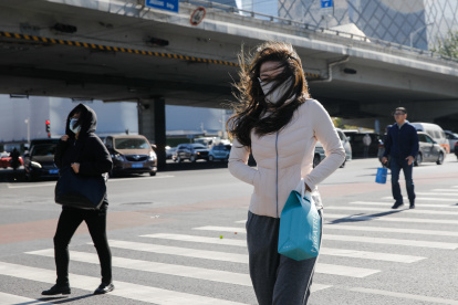 Pekín. Varias personas transitan una calle de esta capital en medio de una ola de frío y fuertes vientos.