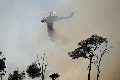 Un helipcótero lanza agua sobre una zona afectada por el fuego, que comenzó en una plantación de pinos en el barrio de Gnangara, un área rural y residencial del noreste de Perth.