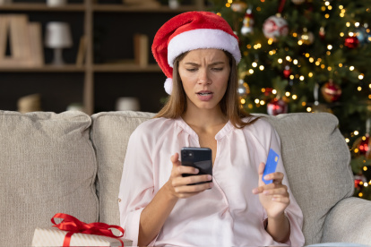 Worried concerned girl in Christmas Santa hat having problems with payment by credit card online for New Year purchases, looking at smartphone screen with puzzled face. Scam, fraud concept