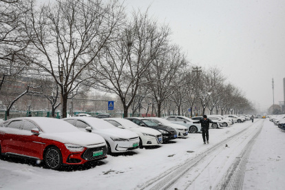 Un hombre transita por una calle en donde los carros aparecen estacionados y cubiertos bajo un manto blanco y congelado, en Pekín, este miércoles 13 de diciembre de 2023.