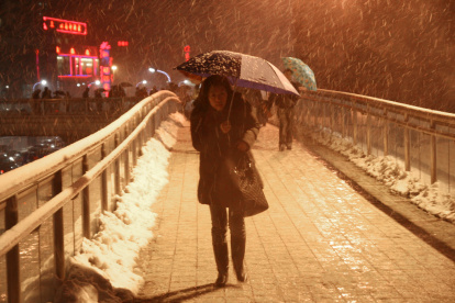 Una mujer al caminar con dificultad sobre un puente peatonal elevado y bajo una fuerte torementa de nieve en Shanghái (China).