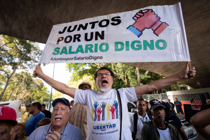 Un trabajador carga una pancarta que dice "juntos por un salario digno" durante una protesta para exigir aumento salarial y de pensiones, hoy, en Caracas (Venezuela).