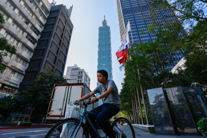 Un ciclista circula junto a una bandera de Taiwán en una calle desde la que se ve el rascacielos Taipei 101, el 12 de enero de 2024, un día antes de las elecciones presidenciales.