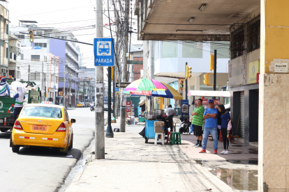 Espacios. Usuarios de buses se protegen de los rayos solares en los exteriores de un inmueble en el centro de Guayaquil mientras esperan por sus unidades.