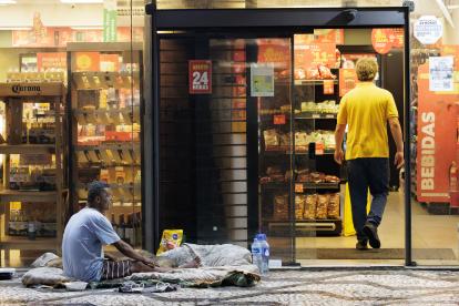 Desigualdades. Una persona en condición de calle espera ayuda de transeúntes afuera de un minimercado.