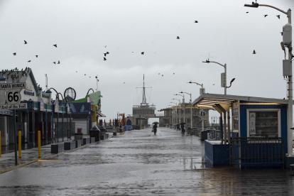 Una persona recorre el muelle de Santa Mónica sosteniendo un paraguas en medio la tormenta azota el sur de California.