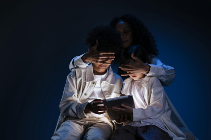 Una par de niños son contralados por una persona mayor, para evitar que sigan vinculados con un dispositivo electrónico.