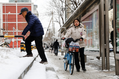 La gente espera un autobús en la calle después de una Nevada en Beijing, China, 21 de febrero de 2024.