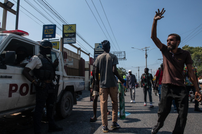 Manifestantes contra la situación política y social de Haití tras la renuncia del primer ministro Ariel Henry pasan junto a un carro policial.