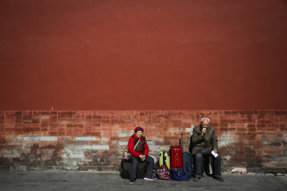 Una pareja de ancianos espera junto a su equipaje durante una visita a la Ciudad Prohibida en Pekín