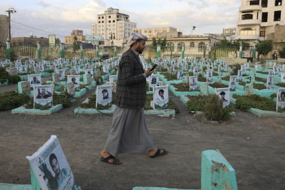 Un partidario hutí pasa junto a las tumbas de los combatientes hutíes en un cementerio dedicado a aquellos que murieron en la prolongada guerra del país, antes del noveno aniversario de la intervención saudí en la guerra de Yemen, en Saná, Yemen.
