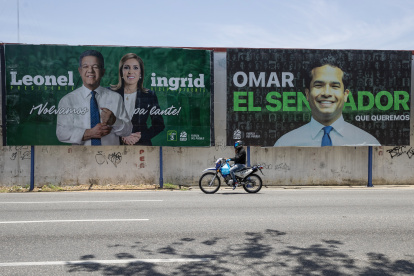Una persona en una motocicleta pasa junto a un cartel de campaña electoral este domingo, en Santo Domingo (República Dominicana).