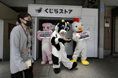 Activistas vestidos como un pollo, un cerdo y una vaca sostienen carteles que dicen "Cada animal es alguien", frente a una tienda que vende carne de ballena en máquinas expendedoras.