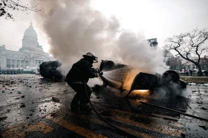 Un bombero apaga un auto en llamas durante enfrentamientos entre la policía y personas que protestan a las afueras del senado durante un debate este miércoles, en Buenos Aires (Argentina). Manifestantes y policías protagonizan un choque este miércoles a las puertas del Senado de Argentina mientras la cámara legislativa debate la ley de Bases, el proyecto estrella del Gobierno, con el que el presidente Javier Milei pretende implementar un paquete de reformas económicas de gran calado. EFE/ Juan Ignacio Roncoroni