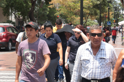 Soleado. Varias personas acelerando el paso en una calle principal de Guayaquil, para evitar el fuerte sol.