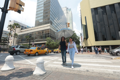 Un para de personas atraviesa una calle de Guayaquil en un día de mucho sol.