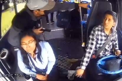 Uno de los tres delincuentes que se subieron al bus amenaza al conductor y a la pasajera que estaba junto a él