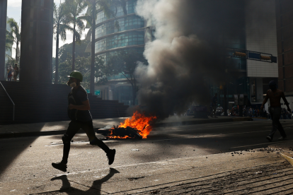 Un manifes.tante corre durante enfrentamientos entre opositores y miembros de la Guardia Nacional Bolivariana (GNB)