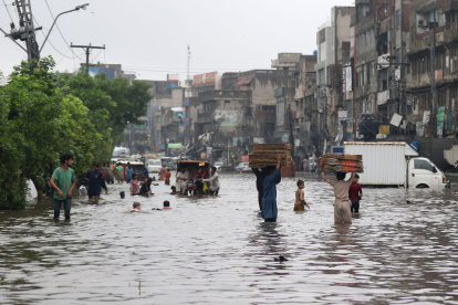 Personas y vehículos avanzan por una calle inundada después de fuertes lluvias en Lahore, Pakistán, el 1 de agosto de 2024.