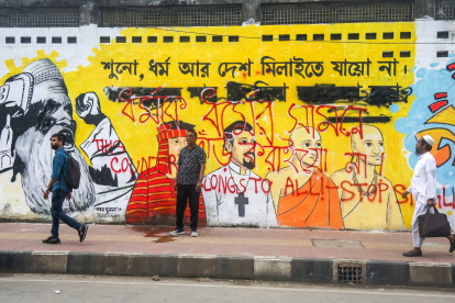 Varias personas caminan junto a un mural en una calle de Daca.