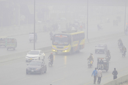 Personas viajan en coches y motocicletas bajo la nube de contaminación en Lahore.