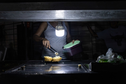 Una persona vende comida ayudado con un bombillo en medio de la oscuridad durante un corte eléctrico, el 29 de febrero de 2024 en Maracaibo.