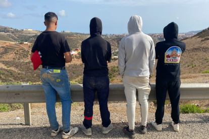 Adam (d) y otros jóvenes miran hacia Ceuta en una carretera a un kilómetro de Fnideq (Castillejos).