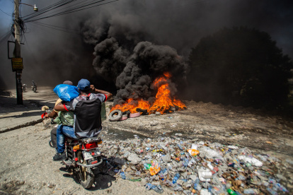 Puerto Príncipe. Dos hombres pasan frente a barricada con fuego.