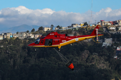 Fotografía de un helicóptero de bomberos lanzando agua para extinguir un incendio el 12 de septiembre de 2024 en las laderas del cerro El Panecillo, ubicado en el centro Histórico de Quito (Ecuador).