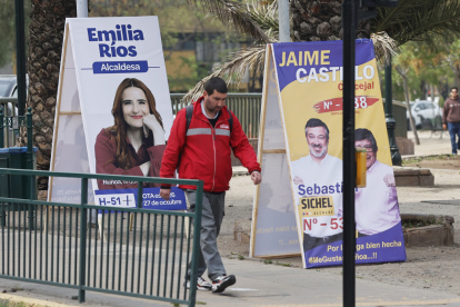 Un hombre camina frente a un afiche con propaganda electoral.