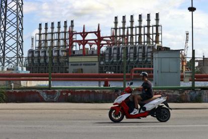 Un hombre en una moto eléctrica pasa frente a una de las plantas de generación eléctrica que permanece este domingo 20 de octubre, en el puerto de La Habana (Cuba).