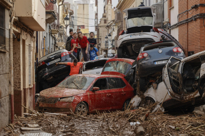 Vecinos de Paiporta intentan pasar entre una montonera de vehículos arrastrados por la corriente, este viernes.
