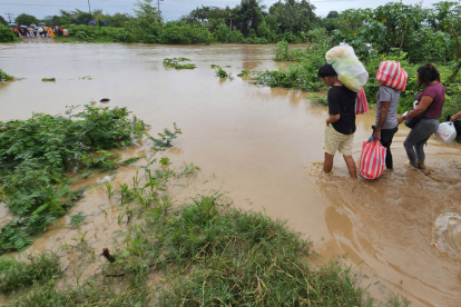 personas cruzan con sus pertenencias por un río en medio de las inundaciones causadas por la tormenta tropical Sara en El Progreso, Honduras.