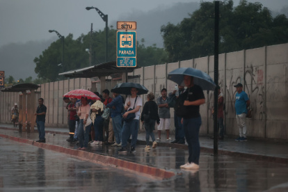 Decenas de usuarios con paraguas permanecen la tarde de este 12 de diciembre a un costado de las vías.