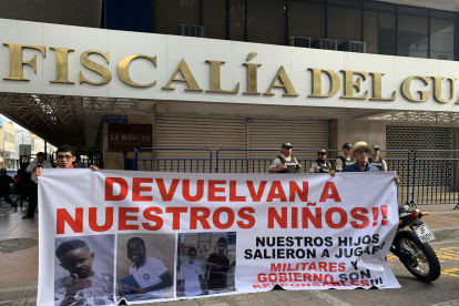 Luis Arroyo (d) y Josué Arroyo (i), padre y hermano de un menor desaparecido, sostienen un cartel con la foto de sus familiares en los exteriores de la Fiscalía Provincial del Guayas en Guayaquil.