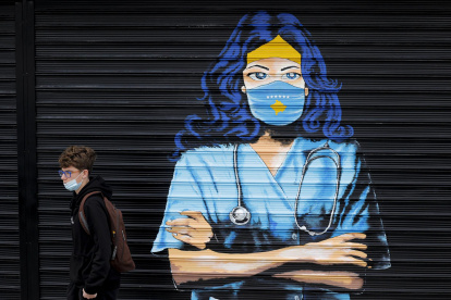 Un chico con mascarilla pasa delante de un mural en Pristina (Kosovo)