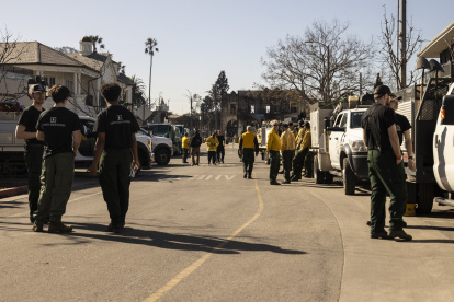 Un edificio carbonizado se ve a lo lejos mientras los empleados de una compañía privada de extinción de incendios, trabajan.