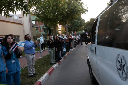 Personas y personal del Centro Médico Shamir frente al complejo hospitalario de Beer Yaakov, ondean banderas mientras llegan ambulancias de la policía que transportan a cinco rehenes recién liberados.