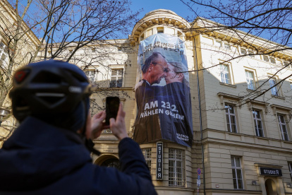 Un hombre toma una fotografía del cartel que muestra el inicio de un beso entre el favorito de las encuestas, el líder conservador Friedrich Merz, y la candidata ultraderechista Alice Weidel, en Berlín, el 20 de febrero de 2025.