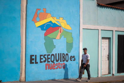 Transeúntes caminando frente a un mural con el mapa de Venezuela que dice "El Esequibo es nuestro", en Caracas.
