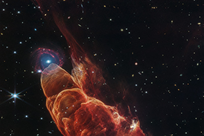 el telescopio espacial James Webb. La nube de forma cónica de color rojo anaranjado corresponde a Herbig-Haro 40/50, en el extremo superior izquierdo hay una galaxia de fondo en forma de espiral con un centro azul.